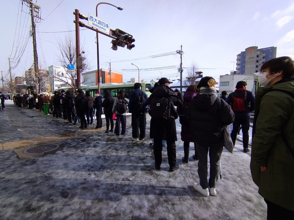 金閣寺の雪化粧を見ようとバス停（西院）に並ぶ人々